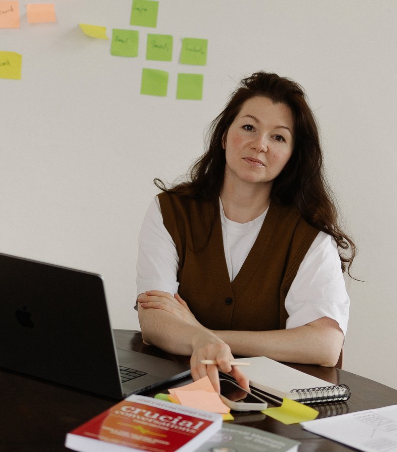 Karina at her desk with a laptop, sticky notes on the wall behind her